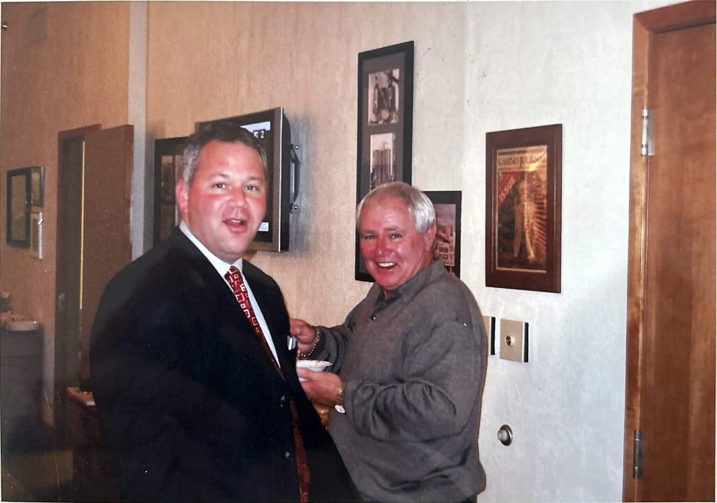 Stephen Crystal and Dave Barrick laughing together in an office hung with framed casino memorabilia.
