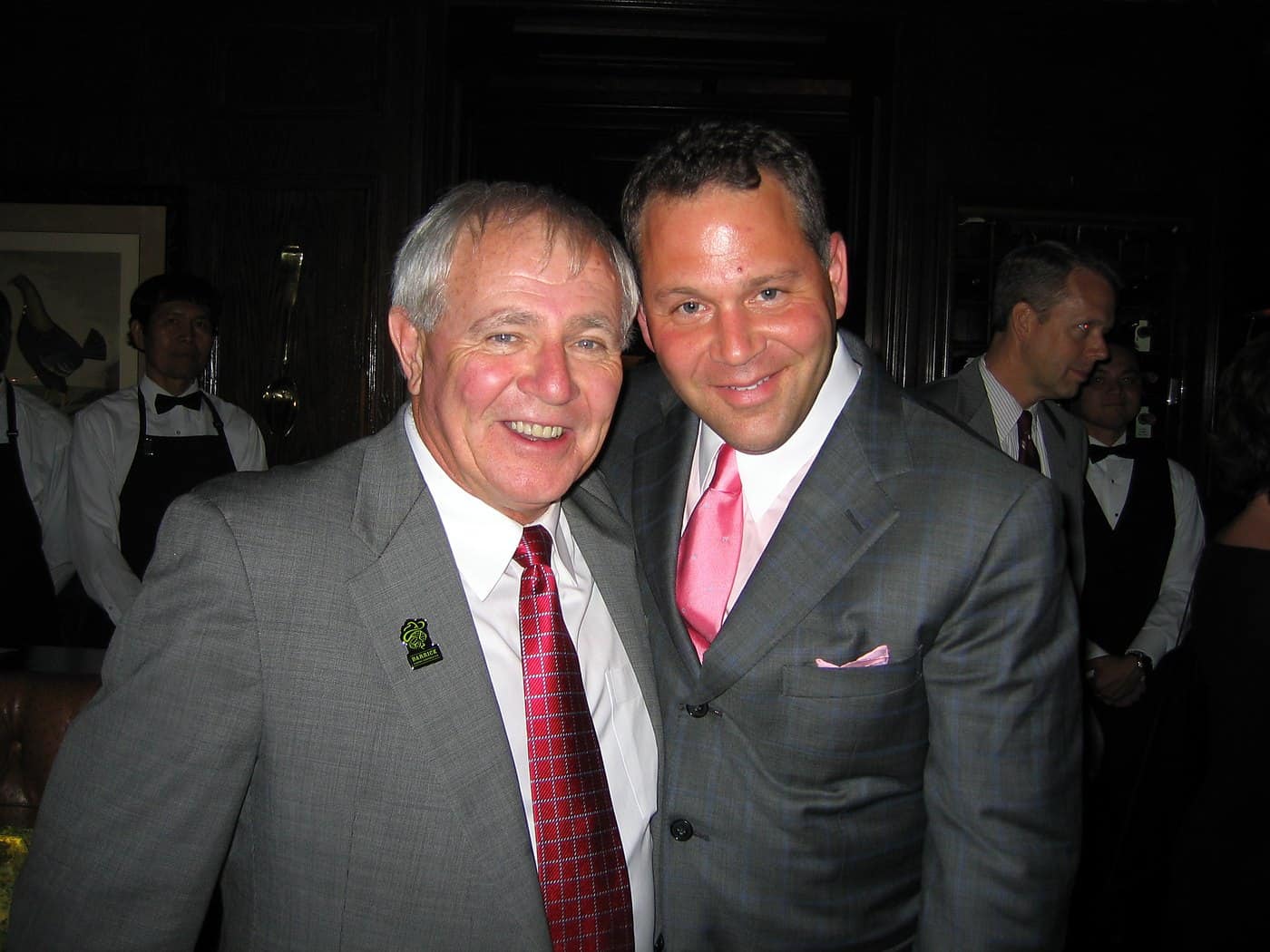 Dave Barrick and Stephen Crystal with arms around each other's shoulders, both laughing, at an evening dinner.