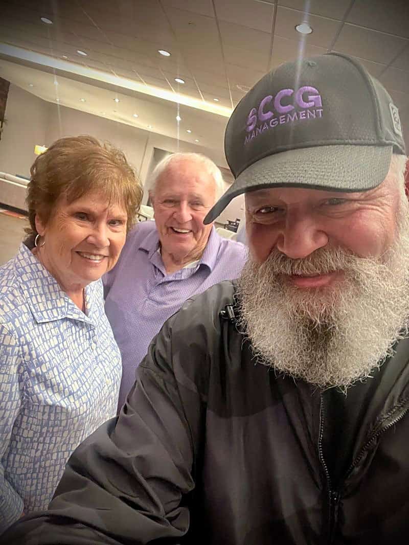 Three people leaning in together for a close, informal photograph; one wears an SCCG Management cap.